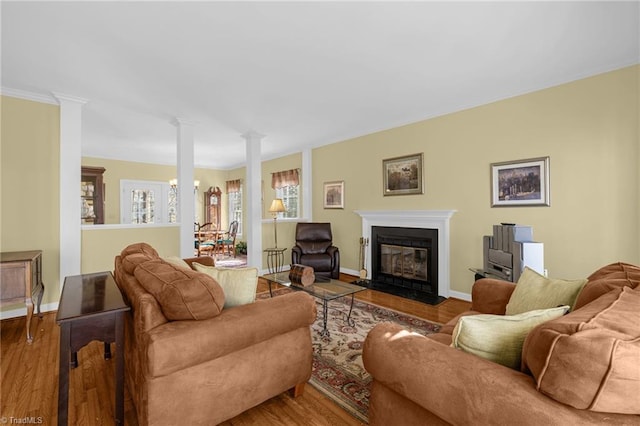 living room with ornate columns, a fireplace with flush hearth, baseboards, and wood finished floors