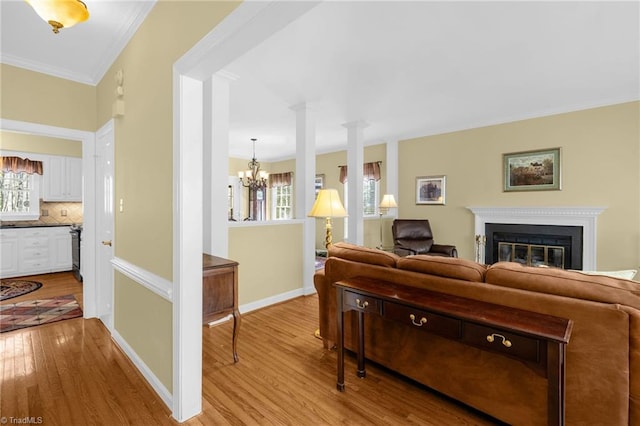 living room with ornamental molding, a glass covered fireplace, a chandelier, light wood-type flooring, and baseboards