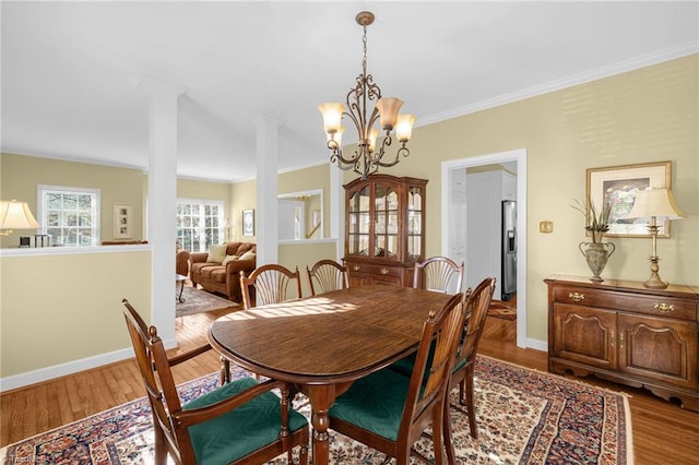 dining area featuring crown molding, light wood-type flooring, decorative columns, and baseboards