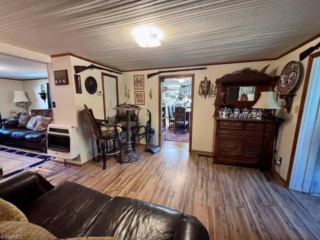 living area with heating unit, baseboards, crown molding, and wood finished floors