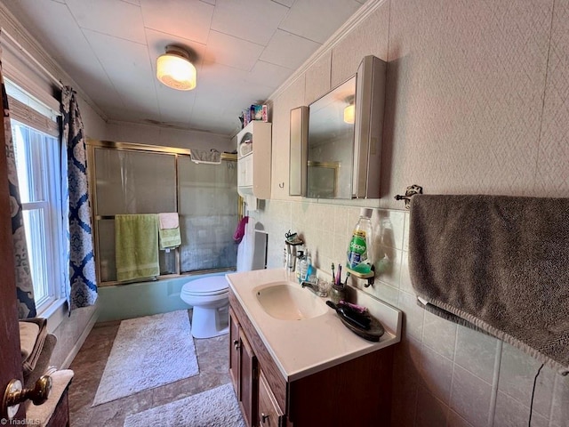 bathroom with crown molding, tile walls, vanity, combined bath / shower with glass door, and toilet