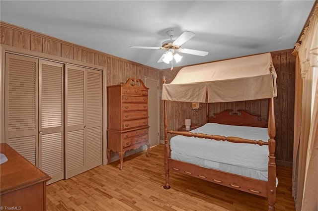 bedroom with ceiling fan, a closet, light hardwood / wood-style floors, and wood walls