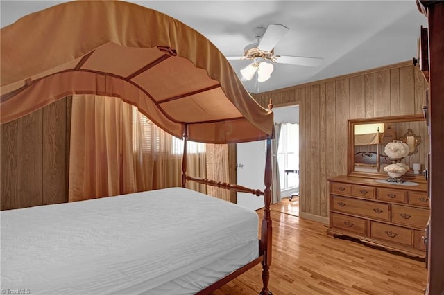 bedroom with ceiling fan, wood walls, and light hardwood / wood-style flooring