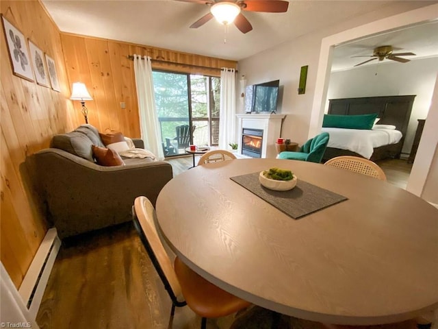dining area with wood walls, a glass covered fireplace, a ceiling fan, and a baseboard radiator