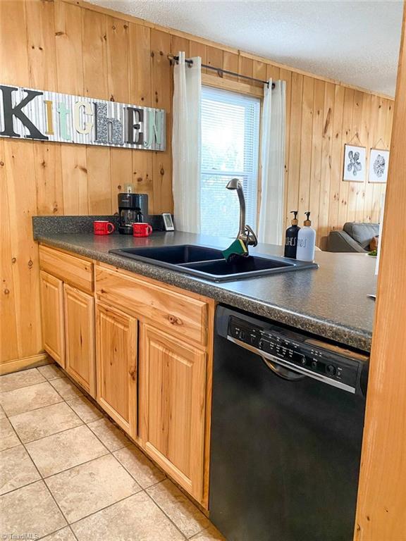 kitchen with black dishwasher, dark countertops, a sink, and a textured ceiling