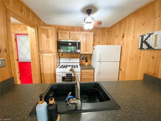 kitchen featuring white appliances, a textured ceiling, dark countertops, wooden walls, and light brown cabinets