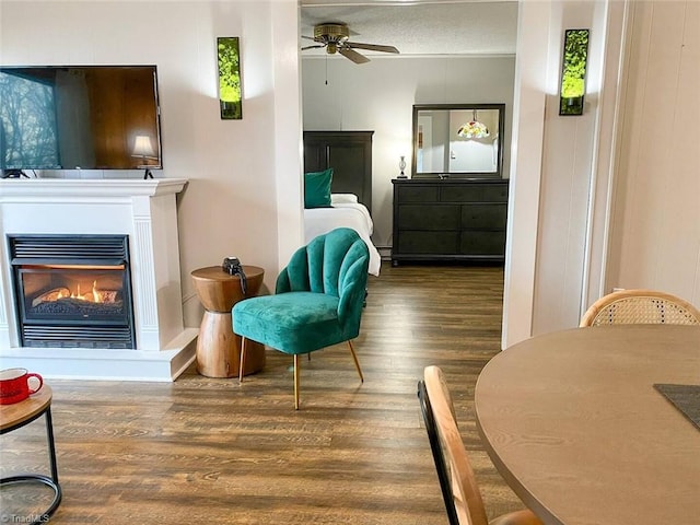 sitting room featuring a textured ceiling, wood finished floors, a glass covered fireplace, and a ceiling fan