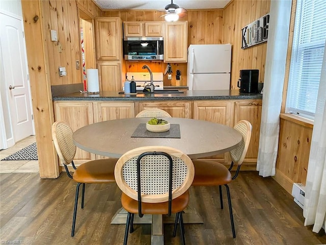 kitchen featuring wood walls, stainless steel microwave, dark wood finished floors, freestanding refrigerator, and light brown cabinets