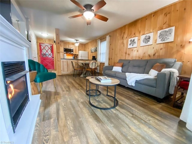 living area featuring a ceiling fan, wooden walls, and wood finished floors