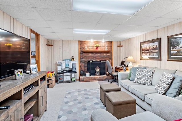 living area featuring light carpet, a brick fireplace, a drop ceiling, and wood walls