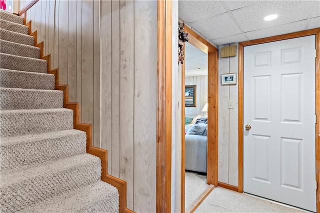 stairway featuring carpet flooring, a paneled ceiling, and wooden walls