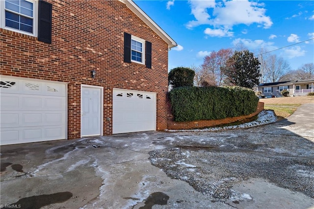 view of side of property with driveway, an attached garage, and brick siding