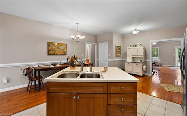 kitchen with a chandelier, brown cabinetry, light countertops, a sink, and light tile patterned flooring