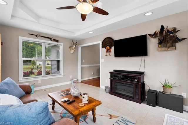 living area featuring recessed lighting, tile patterned floors, ceiling fan, baseboards, and a tray ceiling
