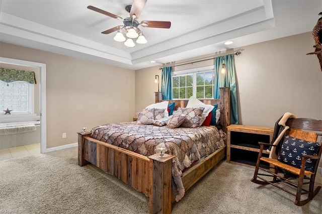bedroom featuring connected bathroom, a raised ceiling, baseboards, carpet, and a ceiling fan