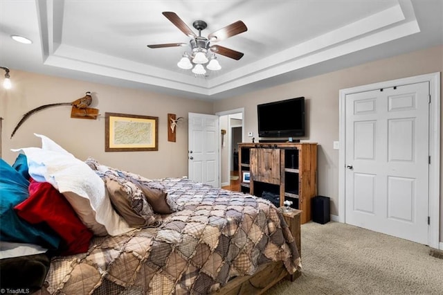 bedroom with a ceiling fan, carpet floors, and a tray ceiling