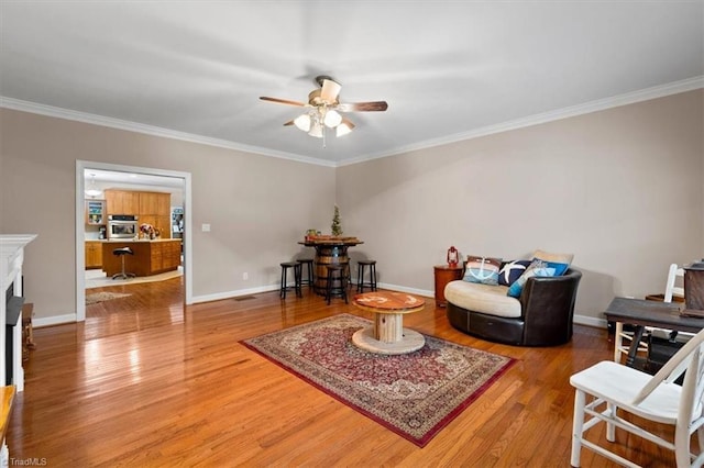 sitting room featuring a fireplace, crown molding, a ceiling fan, baseboards, and wood finished floors