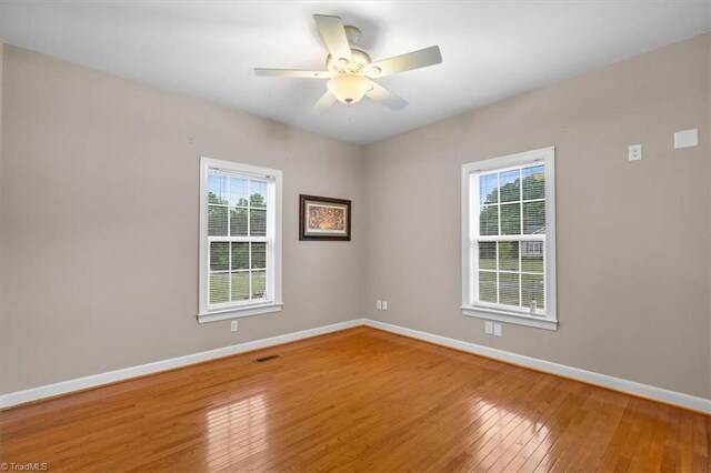 empty room featuring visible vents, plenty of natural light, hardwood / wood-style floors, and baseboards
