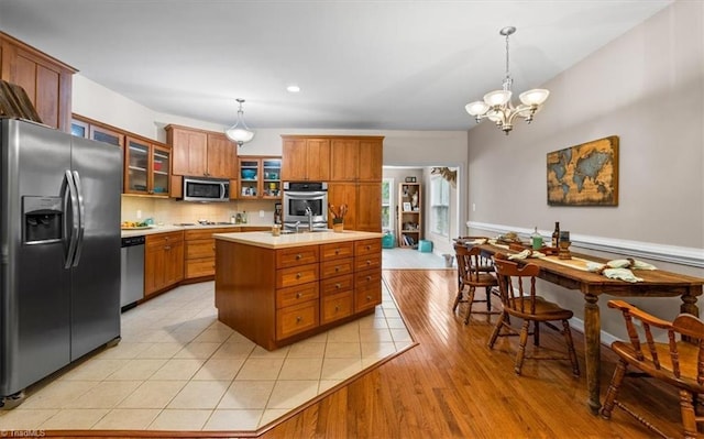 kitchen with an island with sink, brown cabinets, stainless steel appliances, and light countertops