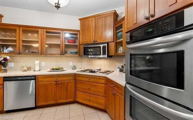 kitchen with decorative backsplash, appliances with stainless steel finishes, light countertops, brown cabinets, and light tile patterned flooring