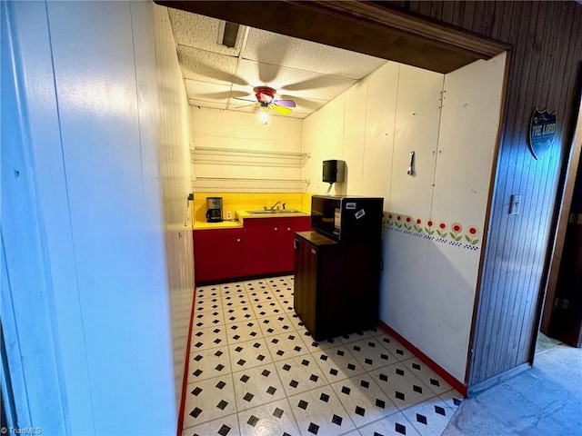 kitchen featuring ceiling fan, wood walls, and sink