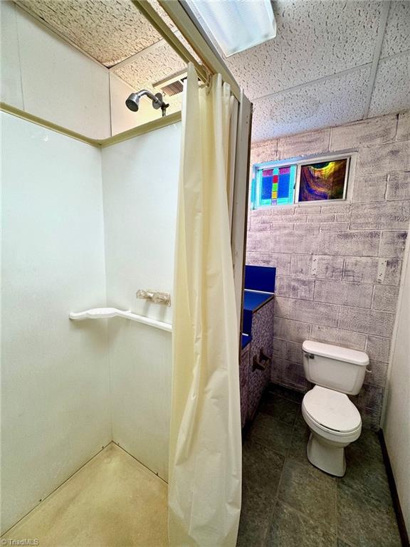 bathroom featuring toilet, a drop ceiling, and walk in shower