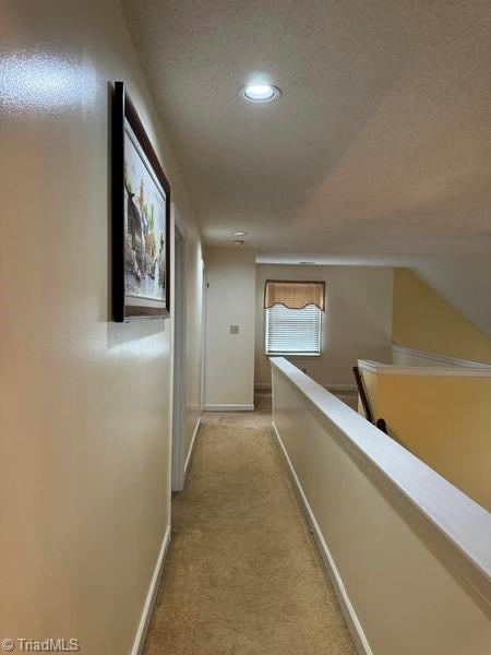 hall with baseboards, light carpet, a textured ceiling, and an upstairs landing