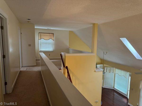 hall with an upstairs landing, vaulted ceiling with skylight, a textured ceiling, and baseboards