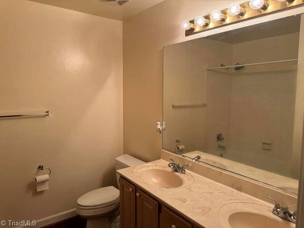 full bathroom featuring double vanity, toilet, baseboards, and a sink