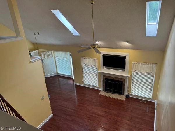 unfurnished living room featuring baseboards, lofted ceiling with skylight, a fireplace with flush hearth, wood finished floors, and a ceiling fan