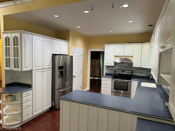 kitchen featuring under cabinet range hood, stainless steel appliances, dark countertops, and a sink