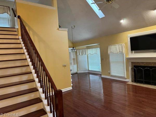 interior space with stairway, wood finished floors, high vaulted ceiling, a fireplace with flush hearth, and ceiling fan