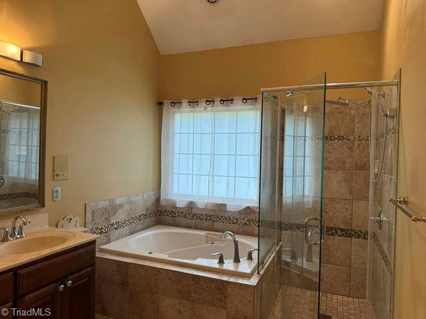 full bath with a shower stall, vanity, a garden tub, and vaulted ceiling