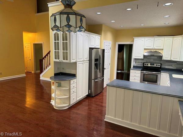 kitchen with dark countertops, extractor fan, dark wood-style floors, white cabinets, and stainless steel appliances