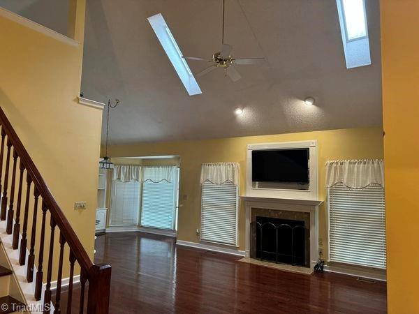 unfurnished living room featuring wood finished floors, high vaulted ceiling, a fireplace with flush hearth, ceiling fan, and stairs