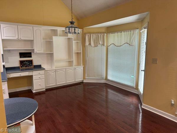 kitchen featuring vaulted ceiling, built in desk, hanging light fixtures, white cabinetry, and open shelves