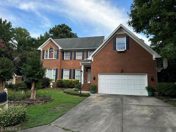 colonial inspired home with concrete driveway, a garage, brick siding, and a front yard