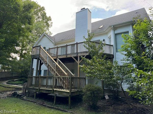 back of house with a chimney, a wooden deck, stairs, and roof with shingles