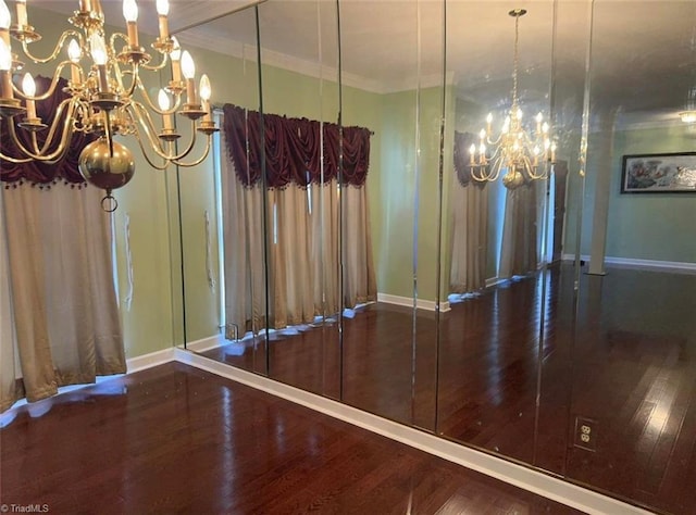 unfurnished dining area with baseboards, a notable chandelier, wood finished floors, and crown molding