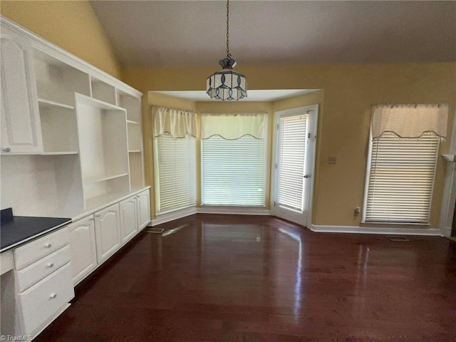 unfurnished dining area featuring dark wood finished floors, vaulted ceiling, and baseboards