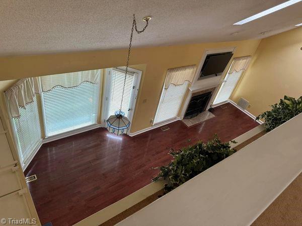 unfurnished living room with a fireplace with flush hearth, wood finished floors, baseboards, and a textured ceiling