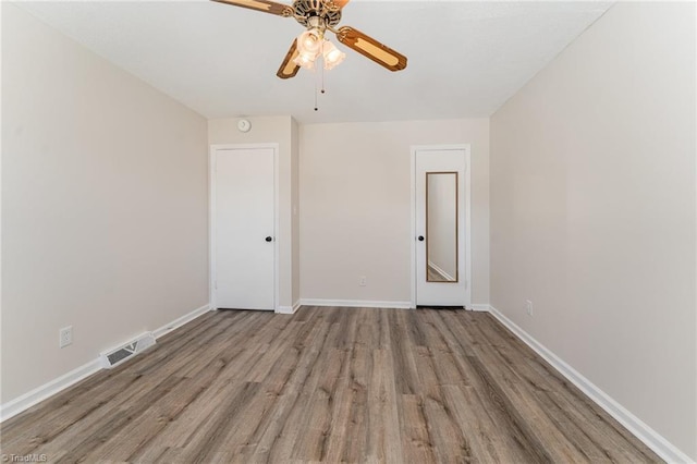 unfurnished room with a ceiling fan, wood finished floors, baseboards, and visible vents