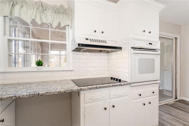 kitchen featuring backsplash, oven, under cabinet range hood, white cabinetry, and black electric cooktop