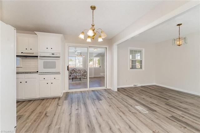 unfurnished dining area with light wood finished floors, an inviting chandelier, baseboards, and a wealth of natural light