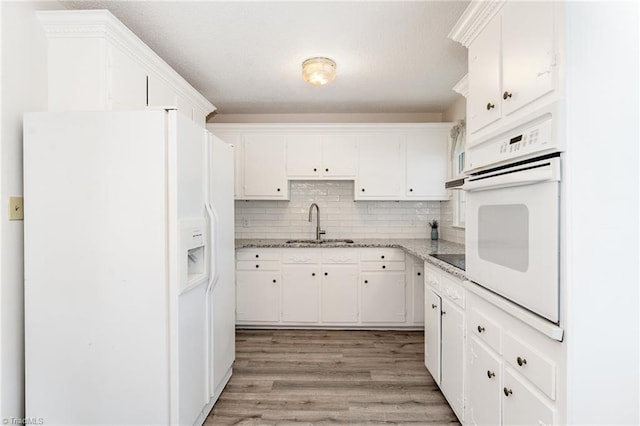 kitchen featuring white appliances, light wood-style flooring, a sink, white cabinets, and backsplash