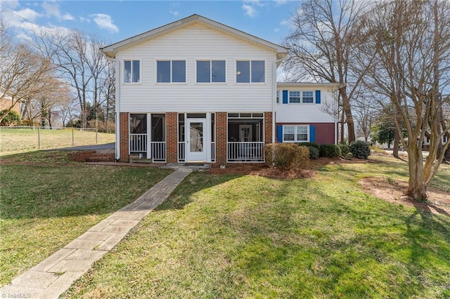 view of front facade with fence, brick siding, a front lawn, and a sunroom