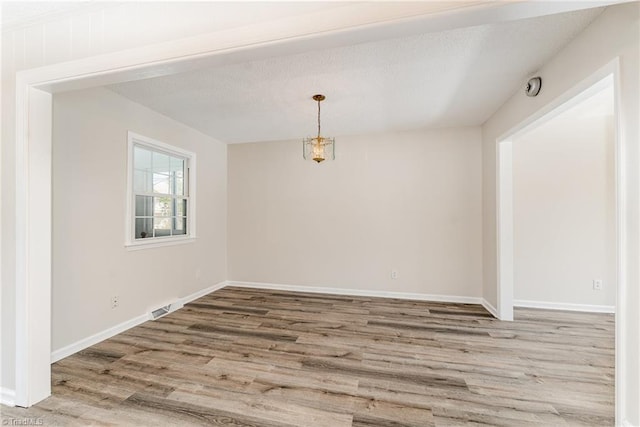 empty room with visible vents, a textured ceiling, and wood finished floors