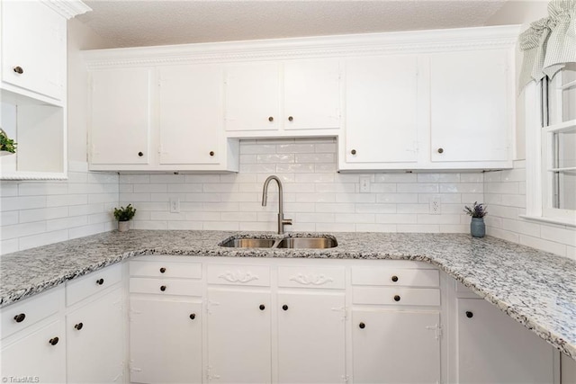 kitchen with decorative backsplash, white cabinets, light stone countertops, and a sink