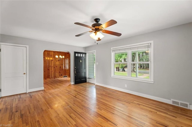 empty room featuring arched walkways, baseboards, a ceiling fan, and light wood finished floors