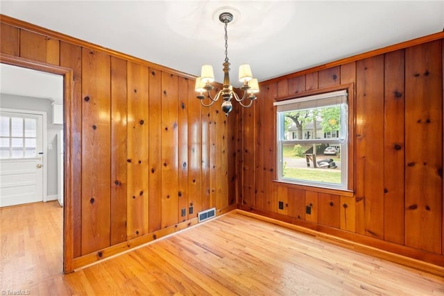 unfurnished dining area with a chandelier, light wood-style flooring, baseboards, and wooden walls